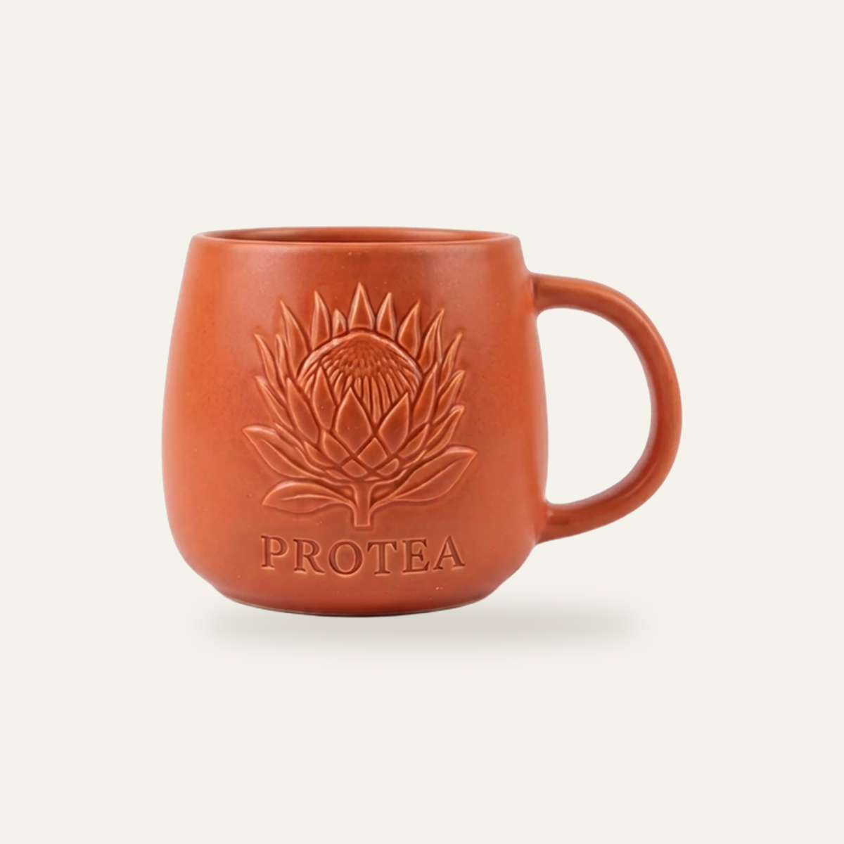 Terracotta stoneware mug photographed straight on, with a protea motif pressed down into the clay surface, the recess catching a soft shadow so the mark reads through light rather than colour
