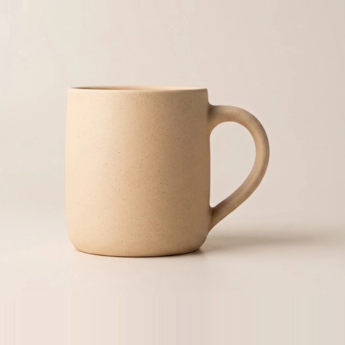 Heavy stoneware mug in a warm sand tone, lightly speckled through the clay, with a thick rounded handle
